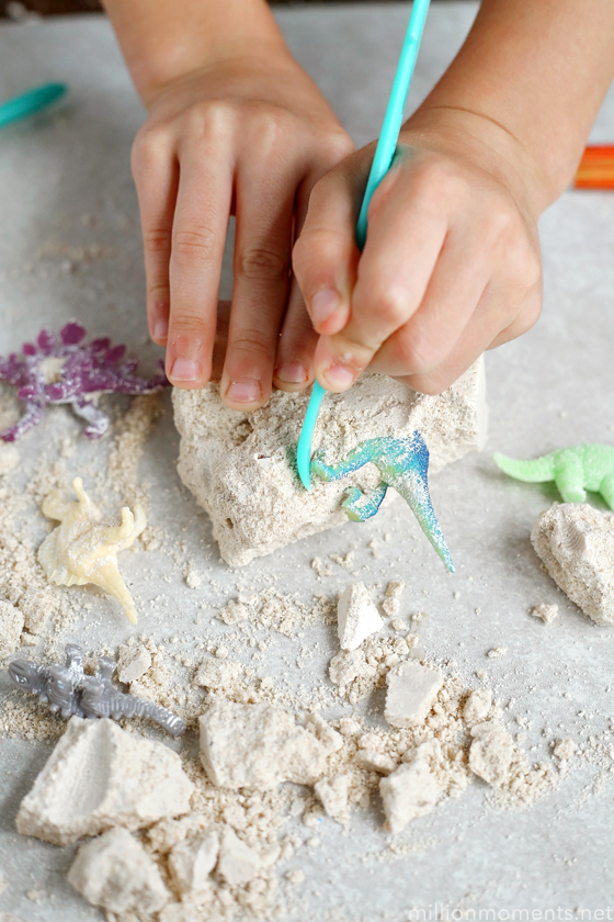 child hands using clay tools to dig plastic dinosaurs out of plaster